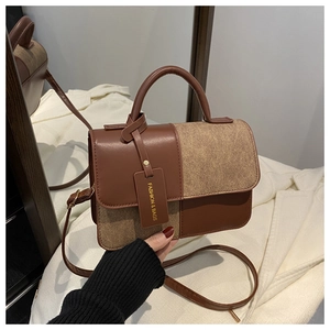 Detail of a textured brown patchwork crossbody bag with metallic logo tag and handle
