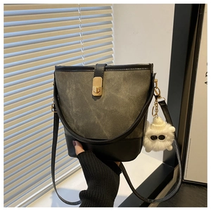 Detail of color-block bucket bag with gold twist lock and a white plush charm accessory
