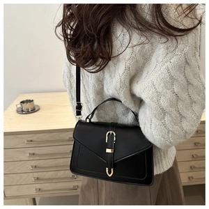Detail of a black leather crossbody bag with gold buckle on a minimalist interior background