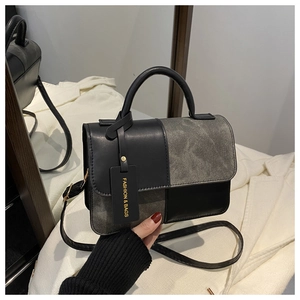 Detail of grey and black patchwork leather handbag with metal brand tag and top handle