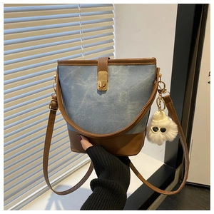 Detail of blue denim bucket bag with brown leather trim and fluffy white keychain charm