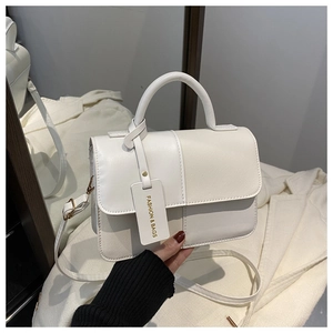 Detail of white patchwork crossbody bag with decorative tag and adjustable strap