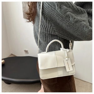 Close-up of ivory crossbody bag with contrast stitching and branded fashion tag