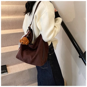 Detail of deep brown suede hobo bag with teddy charm and striped scarf on model