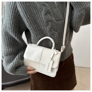 Close-up of white leather crossbody bag with top handle and textured litchi grain finish