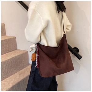 Detailed side view of large brown suede shoulder bag with plush charm and striped scarf