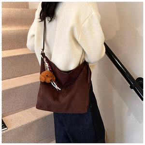 Detail of a dark brown suede tote bag featuring a cute plush bear charm and ribbon