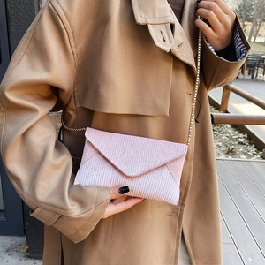 Pink envelope crossbody bag with gold chain strap worn by a model in a trench coat