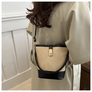Detail of a beige suede and black leather bucket bag with a gold buckle on a model