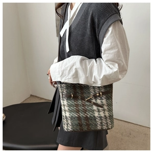 Detail of plaid wool shoulder bag featuring dark green patterns and gold buckle closure