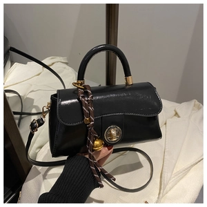 Detail of black glossy handbag with gold twist lock and a decorative bell charm