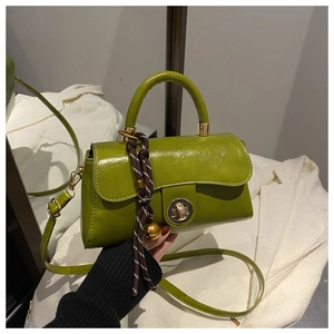 Detail of bright green glossy handbag with gold twist lock and woven charm accessory