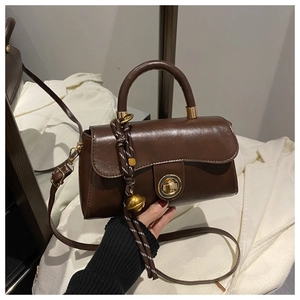 Detailed view of brown leather crossbody bag with gold rotary lock and woven charm detail