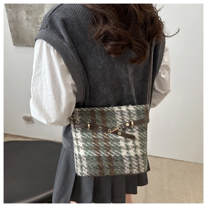 Close-up of green plaid wool crossbody bag with leather strap and golden metal buckle