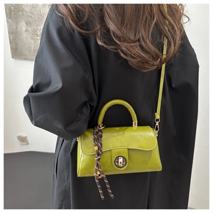 Pea green vintage faux leather handbag with tassel detail shown on a black winter coat