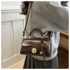 Close-up of brown vintage leather handbag with gold twist lock and woven bell charm