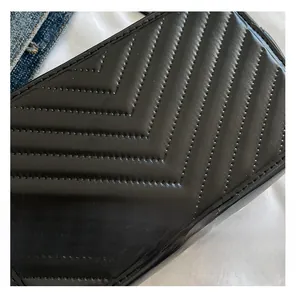 Détail de la texture en cuir noir matelassé avec surpiqûres en V sur un sac bandoulière