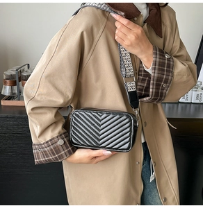 Détail d'un sac caméra noir matelassé avec coutures en V et large bandoulière textile