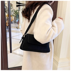 Chic black baguette shoulder bag in matte suede texture worn over a white wool coat