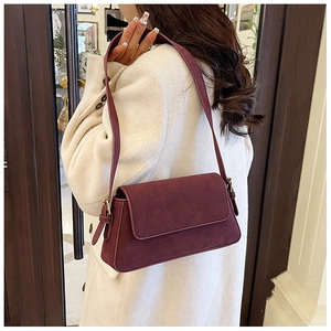 Close-up of matte burgundy suede shoulder bag showing texture and golden buckle details