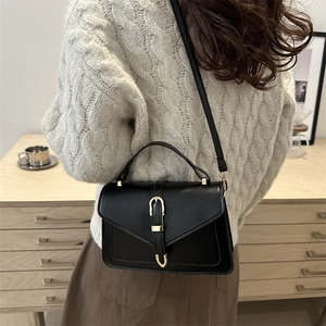 Minimalist black leather handbag with gold horsebit buckle shown on a model