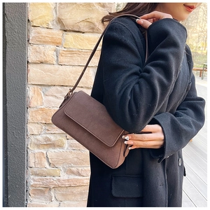 Detail of dark brown baguette shoulder bag in matte suede texture shown outdoors
