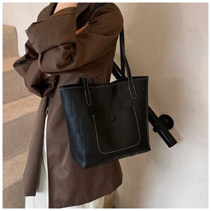 Detail of black tote bag featuring vertical stripes, white stitching, and snap pocket