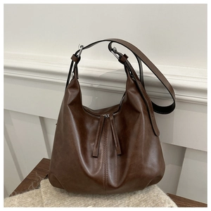 Detail of dark brown leather tote showing vertical stitching and soft texture on wood