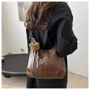 Detail of deep brown retro leather tote bag with cute bear charm on a female model