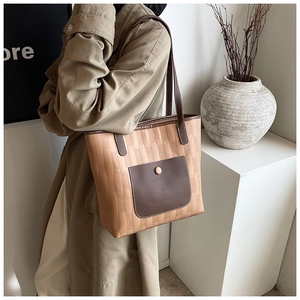 Detail of light brown woven tote bag with dark leather trim and shoulder strap on model