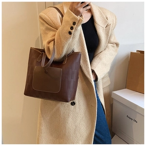 Detail of dark brown tote bag with brick texture pattern and front pocket worn by model