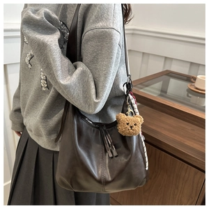 Detail of vintage brown leather tote bag with plush bear charm and silk scarf accent