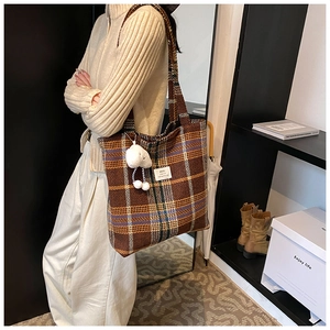 Detail of checkered tweed tote bag with cute white sheep plush pendant on black background