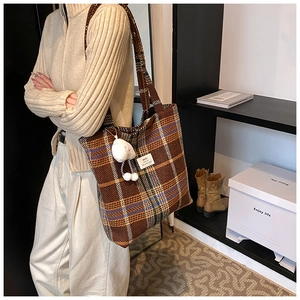 Detailed view of a retro plaid tote bag with a plush lamb pendant on a casual model