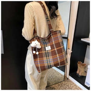 Detail of a brown plaid tote bag featuring a cute white cloud plush pendant and brand tag