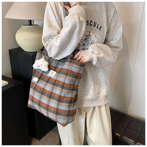 Detail of vintage plaid tote bag with cloud charm accessory worn over shoulder