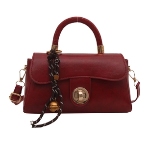 Minimalist deep red square handbag with golden twist lock and woven bell pendant charm