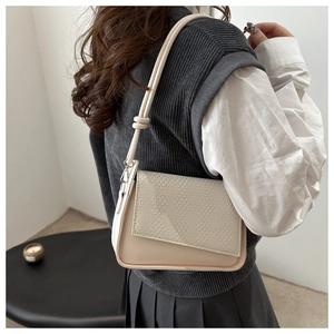 Detail of minimalist beige underarm bag with woven texture flap and knot strap on model