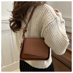 Detail of brown shoulder bag with woven texture flap and knotted strap on shoulder