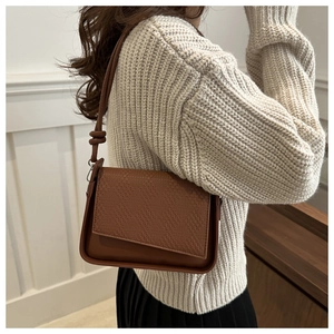 Close-up of brown vintage crossbody bag featuring textured woven flap and knotted strap detail