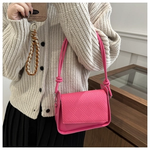 Detail of fuchsia woven crossbody bag with slender rope straps worn on a beige knit sweater