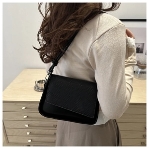 Detail of black underarm bag featuring a delicate woven flap and smooth matte finish