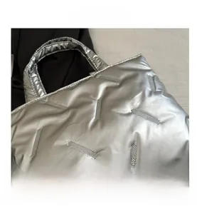 Macro shot of silver quilted puffer tote bag with metallic stripe texture and soft handle