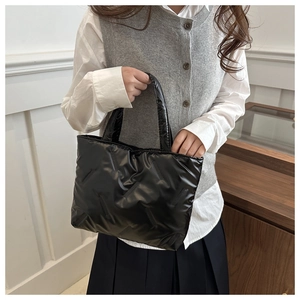 Detail of glossy black quilted tote bag with soft padded texture and minimalist stitching