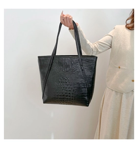 Detailed view of a black crocodile-embossed tote bag worn by a model for a chic look