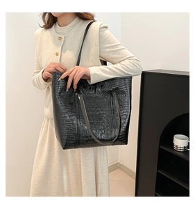 Detail of black faux leather tote bag with crocodile texture and slim shoulder straps