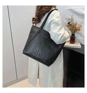 Detail of black crocodile texture tote bag worn on shoulder with stylish beige coat