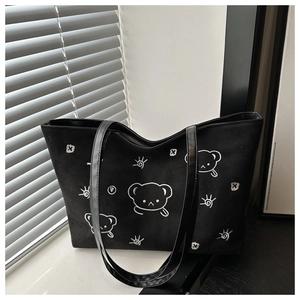 Detail of black tote bag showing white embroidered cartoon bear and sun doodle pattern