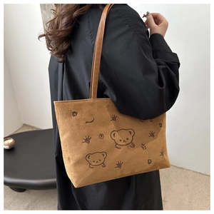 Close-up of brown suede tote bag featuring embroidered cartoon bears and slim shoulder straps
