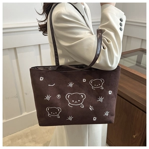 Detail of dark brown tote bag featuring white cartoon bear embroidery and durable shoulder strap